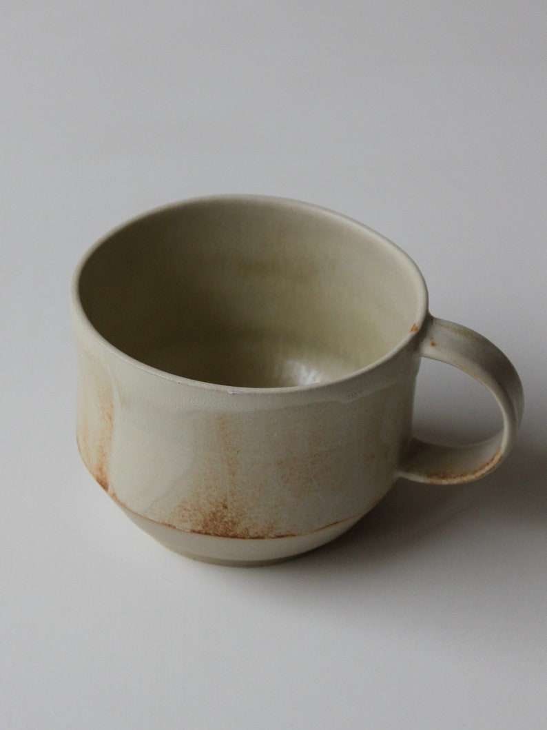 May include: A beige ceramic mug with a brown glaze and a rounded handle.