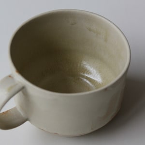 May include: A white ceramic mug with a rounded shape and a handle. The mug has a light brown glaze and a slightly textured surface.