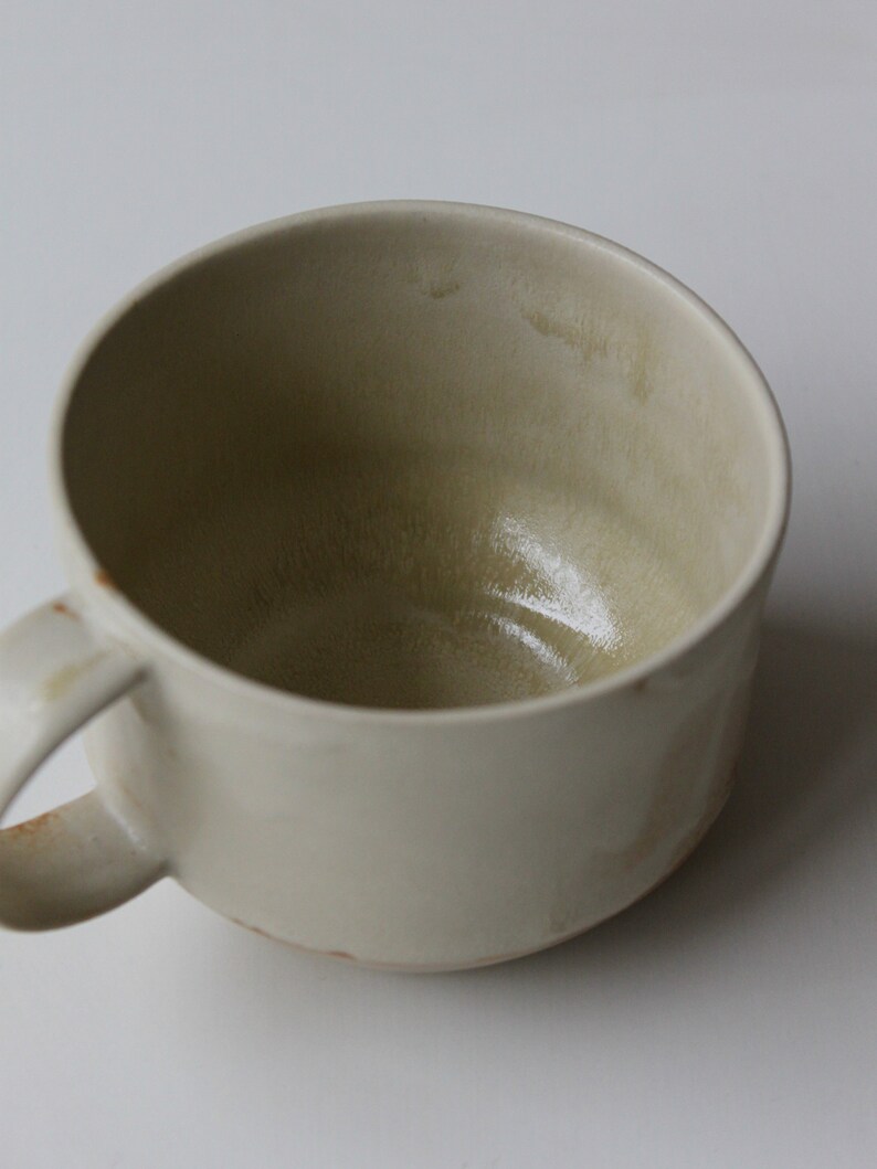 May include: A white ceramic mug with a rounded shape and a handle. The mug has a light brown glaze and a slightly textured surface.