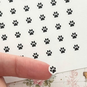 May include: A sheet of white sticker paper with black paw print stickers. The stickers are arranged in a grid pattern.