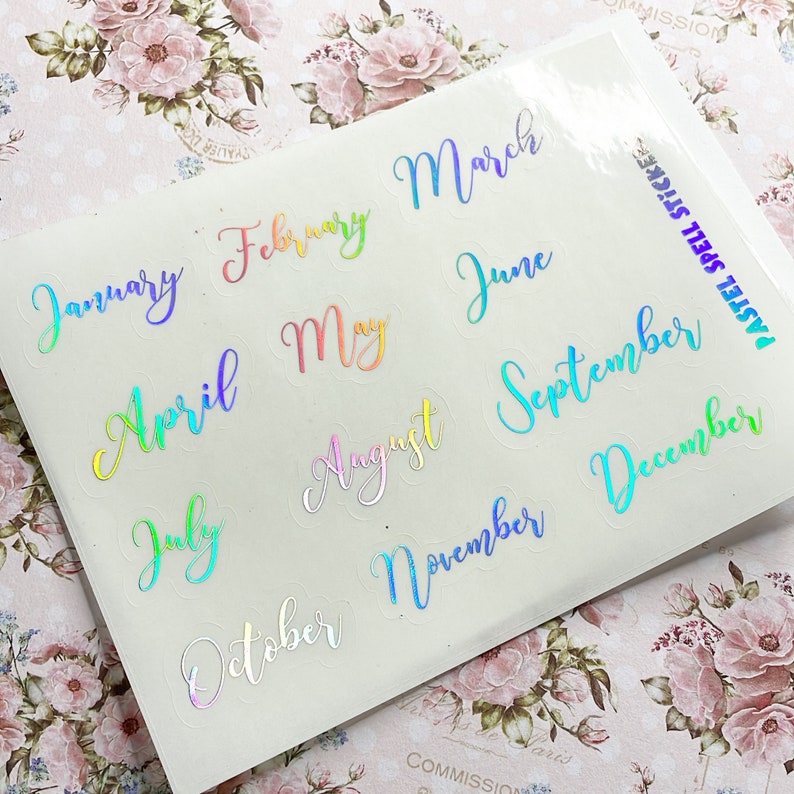 May include: A sheet of pastel holographic stickers with the months of the year written in a cursive font. The stickers are transparent and have a rainbow iridescent finish.