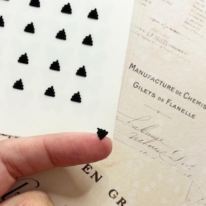 May include: A sheet of black poop stickers. The stickers are arranged in rows and columns on a white background. A finger is holding one of the stickers.