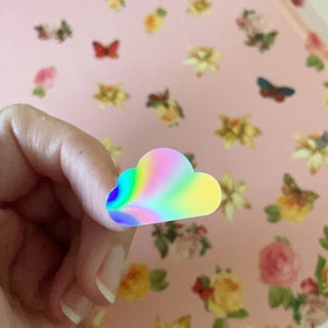 May include: A holographic iridescent rainbow cloud sticker. The sticker is shaped like a cloud and has a rainbow swirl pattern.