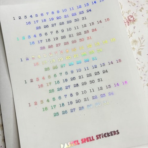 May include: A sheet of pastel holographic stickers with numbers 1 through 31. The stickers are arranged in rows of 15, with each row starting at a different number. The stickers are iridescent and have a rainbow sheen.