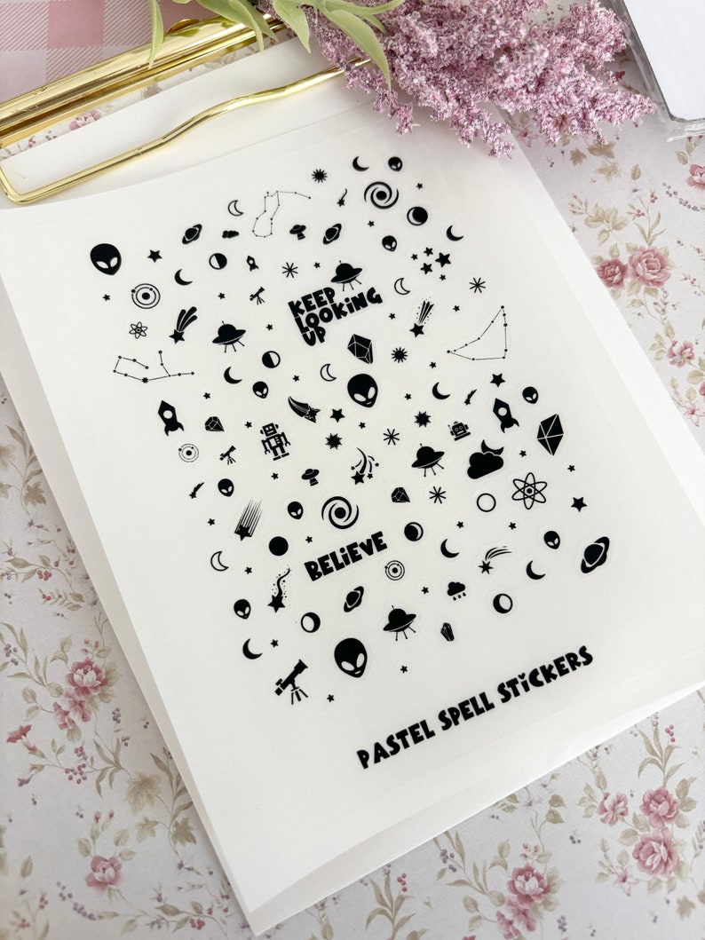 May include: A sheet of pastel spell stickers with a variety of space-themed designs, including aliens, planets, stars, rockets, and the words "Keep Looking Up" and "Believe".