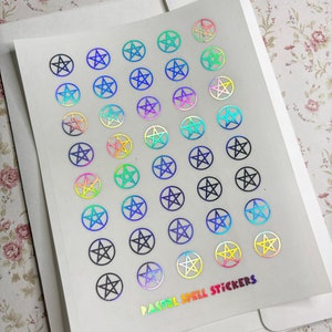 May include: A sheet of pastel holographic pentagram stickers. The stickers are arranged in rows and columns on a white background. The text "PASTEL SPELL STICKERS" is printed in rainbow holographic letters at the bottom of the sheet.