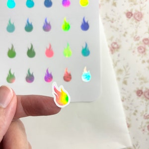 May include: A sheet of 24 iridescent holographic flame stickers. The stickers are rainbow colored and have a glossy finish. The stickers are arranged in a grid pattern on a white sheet.