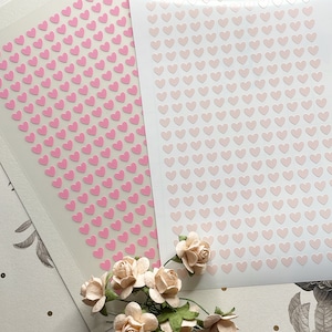 May include: Two sheets of sticker paper with pink hearts. One sheet has a solid pink color and the other sheet has a gradient of pink.