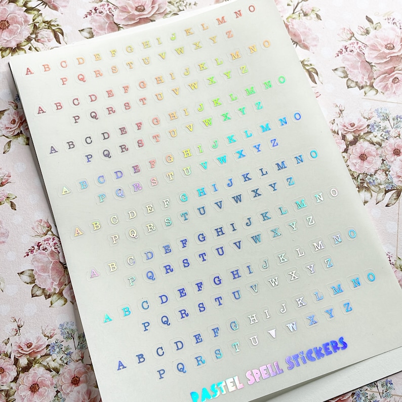 May include: A sheet of pastel colored alphabet stickers with a holographic finish. The stickers are arranged in rows and columns, with each letter appearing multiple times. The sheet is labeled "PASTEL SPELL STICKERS".