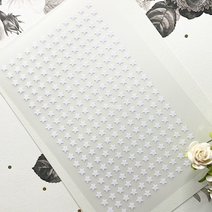 May include: A sheet of white adhesive paper with a repeating pattern of small white stars. The stars are arranged in a staggered pattern.