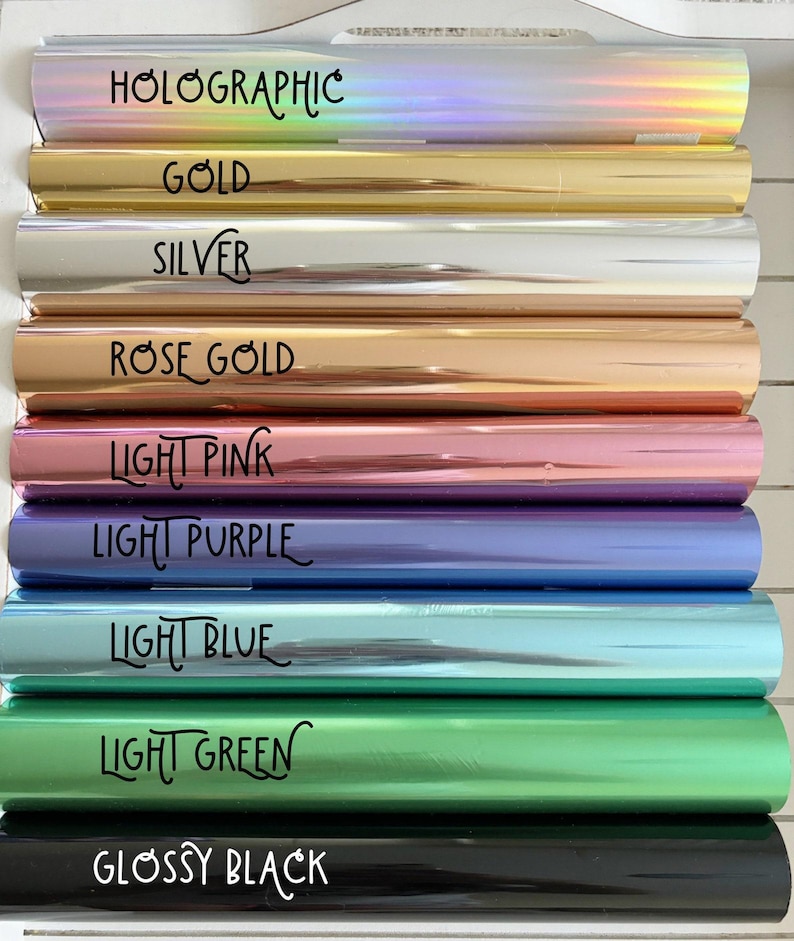May include: A selection of colorful rolls of foil, each labeled with a different color and finish. Colors include holographic, gold, silver, rose gold, light pink, light purple, light blue, light green, and glossy black. The text is in a handwritten style.