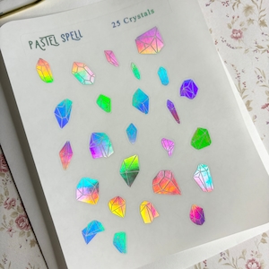 May include: A sheet of stickers featuring 25 holographic crystal designs in various shapes and sizes. The stickers have a rainbow iridescent effect and are labeled "PASTEL SPELL" and "25 Crystals". The crystals are in shades of blue, green, pink, and yellow.
