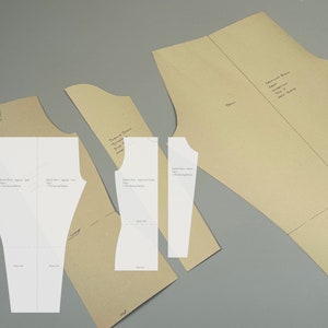 Puede incluir: Un conjunto de patrones de costura para pantalones y una blusa. Los patrones están impresos en papel marrón e incluyen instrucciones para coser las prendas.