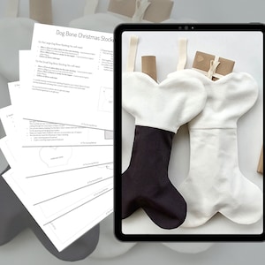 May include: A digital tablet displaying a sewing pattern for a dog bone-shaped Christmas stocking. The pattern includes instructions for cutting and sewing the fabric. Two finished dog bone stockings are shown on a white surface, one white and one black and white.