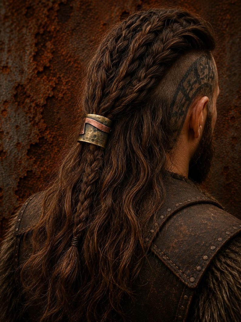 May include: A metallic hair cuff featuring a hammered brass finish with a contrasting copper-colored band. The cylindrical accessory secures a section of long, wavy brown hair that is styled with multiple braids and a shaved side section.