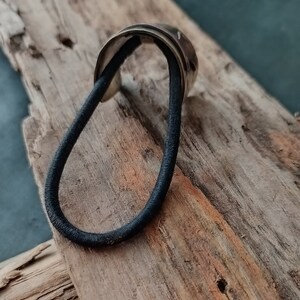 May include: A hair tie featuring a metallic, curved, silver-toned decorative piece attached to a black elastic band. The metallic component has a smooth, reflective surface with subtle indentations along its outer edge, providing a contrast to the simple, circular black elastic cord.