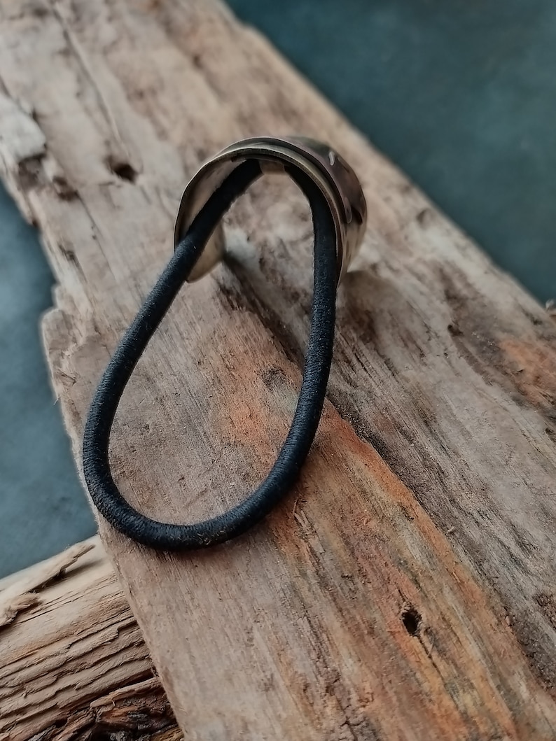 May include: A hair tie featuring a metallic, curved, silver-toned decorative piece attached to a black elastic band. The metallic component has a smooth, reflective surface with subtle indentations along its outer edge, providing a contrast to the simple, circular black elastic cord.