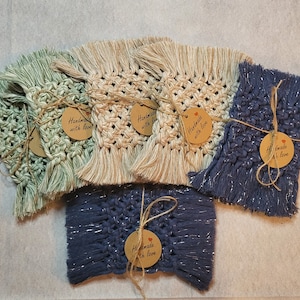 May include: A selection of handmade macrame coasters in shades of green, beige, and blue. Each coaster is tied with twine and a tag that says "Handmade with love."