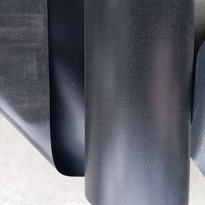 May include: Close-up of a roll of black fabric with a textured, woven pattern. The fabric is tightly rolled, revealing the texture and sheen of the material. The image highlights the fabric's dark color and the detailed weave.