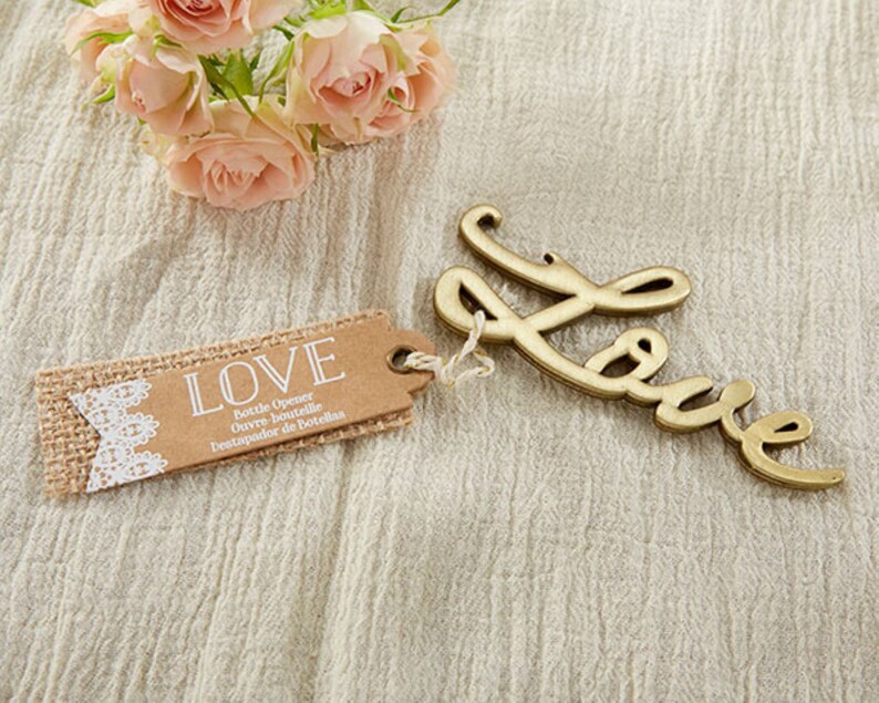 May include: A gold-colored bottle opener shaped like the word "LOVE" with a burlap and lace tag that reads "LOVE Bottle Opener, Ouvre-bouteille, Destapador de Botellas".