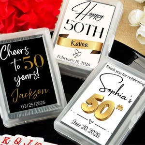 May include: Three personalized playing card decks in clear plastic cases. Each card deck features a different design celebrating a 50th anniversary. The designs include text such as "Cheers to 50 years!", "Happy 50th", and "Thank you for celebrating".