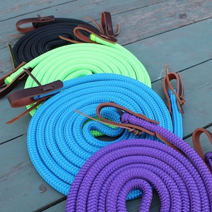 May include: Four coiled horse reins in different colours: black, green, blue, and purple. Each rein has brown leather ends.