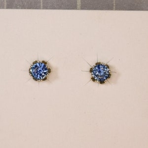 Puede incluir: Un par de pendientes de plata de ley con detalles de piedras preciosas azules. Los pendientes se muestran en una tarjeta blanca con el texto "STERLING SILVER" impreso en ella.