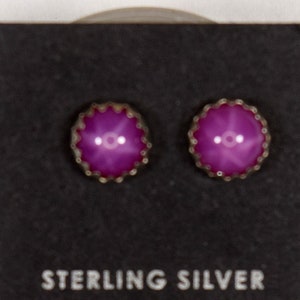 May include: A pair of sterling silver earrings with pink stones set in a silver bezel. The earrings are on a black card with the words "Sterling Silver" printed on it.