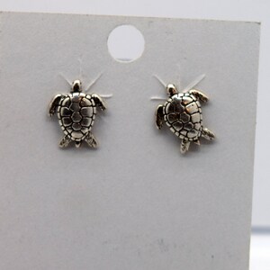 May include: A pair of silver turtle stud earrings on a white card.