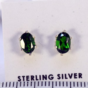 Puede incluir: Pendientes de botón con piedras preciosas verdes esmeralda de corte ovalado, engastados en plata de ley. Los pendientes se muestran sobre una tarjeta blanca con la inscripción "STERLING SILVER" en negro. Una regla está debajo.