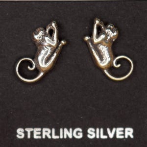 May include: A pair of sterling silver earrings shaped like stylized cats, displayed on a black card. The earrings have a polished finish and a curled tail design. The card reads "STERLING SILVER".