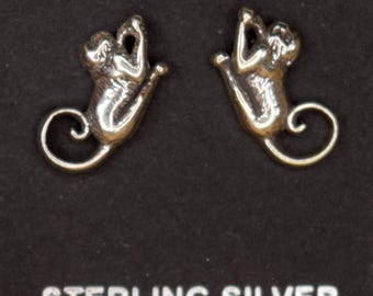 May include: A pair of sterling silver earrings shaped like stylized cats, displayed on a black card. The earrings have a polished finish and a curled tail design. The card reads "STERLING SILVER".