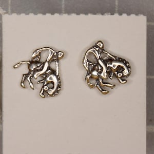 May include: A pair of silver earrings featuring a detailed design of two horses, one standing on top of the other.