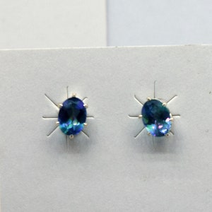 May include: A pair of silver earrings with oval-shaped blue gemstones. The earrings are on a white background.