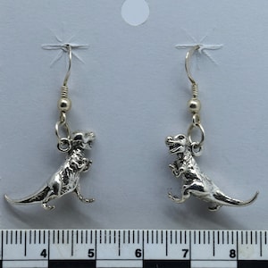 May include: Silver dinosaur earrings with a hook closure. The earrings are approximately 2 inches long.