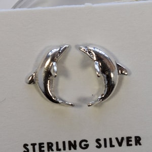 May include: A pair of sterling silver dolphin earrings. The dolphins are facing each other and are in a jumping position.