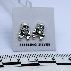 Puede incluir: Un par de pendientes de plata de ley con forma de calavera y huesos cruzados. Los pendientes son pequeños y delicados, y son perfectos para añadir un toque de estilo atrevido a cualquier atuendo.