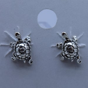 May include: A pair of silver turtle stud earrings. The turtles are facing forward with their legs outstretched.