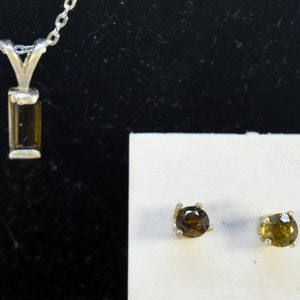 Puede incluir: Un collar de plata con un colgante de piedra preciosa marrón y pendientes a juego de piedra preciosa marrón.