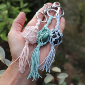 Peut inclure: Trois porte-clés en macramé avec des pierres polies entourées d'un filet en corde nouée et terminées par des pompons assortis. Les pierres sont rose clair, vert sauge et gris foncé, fixées à des mousquetons et anneaux en métal argenté.