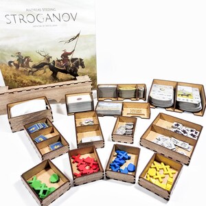 May include: Wooden organizer for the board game "Stroganov" by Mac Gerdts. The organizer includes compartments for cards, tokens, and other game components. The game box is also included in the image.