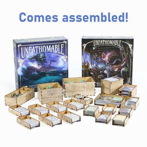Könnte beinhalten: Ein Holzorganizer für das Brettspiel "Unfathomable" mit zwei Spielboxen, eine mit einem blauen und violetten Deckel und die andere mit einem schwarzen und grünen Deckel. Der Organizer wird montiert geliefert und enthält mehrere Fächer zur Aufbewahrung von Spielkomponenten.