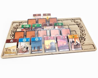 Könnte beinhalten: Ein Holzspielbrett mit einem Lorbeerkranz-Design und Steckplätzen zum Halten von Karten. Das Brett ist gefüllt mit Karten mit verschiedenen Illustrationen und Texten, darunter "Colissey", "Bad", "Theater", "Wachturm", "Fal Gate" und "Taverne".