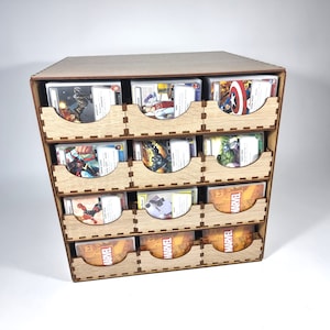 May include: A wooden card organizer with nine compartments, each holding multiple trading cards. The cards feature colorful illustrations of Marvel characters. The organizer is made of light-colored wood and has a simple, geometric design.