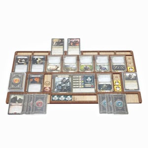 May include: A wooden game organiser with compartments for cards and tokens. The organiser is filled with cards and tokens from a fantasy board game. The cards are arranged in rows and columns, and the tokens are in small compartments. The organiser is made of light brown wood and has a natural finish.