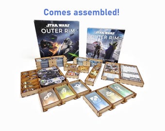 May include: A wooden organizer for the Star Wars Outer Rim board game. The organizer is assembled and includes multiple compartments for storing the game's components. The game's box is visible in the background.