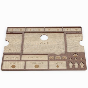 Puede incluir: Un organizador de juegos de madera con compartimentos para cartas, dados y fichas. El organizador tiene una mancha marrón y está etiquetado como "LEADER", "DECK", "DREADS", "TROOPS", "SPICE", "SOLARI", "WATER" y "DISCARD".