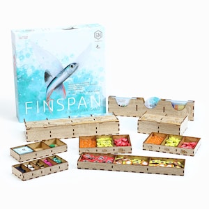 Puede incluir: Organizador de madera para el juego de mesa "Finspan", un juego de Wingspan. El organizador incluye múltiples bandejas con compartimentos para las piezas y las cartas del juego. El arte de la caja presenta un pez volador sobre un fondo azul y blanco.