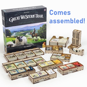 Può includere: Gioco da tavolo "Great Western Trail" con componenti di stoccaggio in legno. La scatola del gioco presenta un'illustrazione del paesaggio con pecore e un cowboy. Il testo "Comes assembled!" è anche visibile.