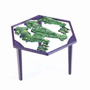 Può includere: Un tavolo esagonale con gambe viola e un piano in vetro trasparente. Il piano del tavolo presenta un design di diverse astronavi verdi e gialle.